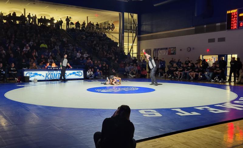 A spotlight shines on the Kasson-Mantorville mat during a high school wrestling match.