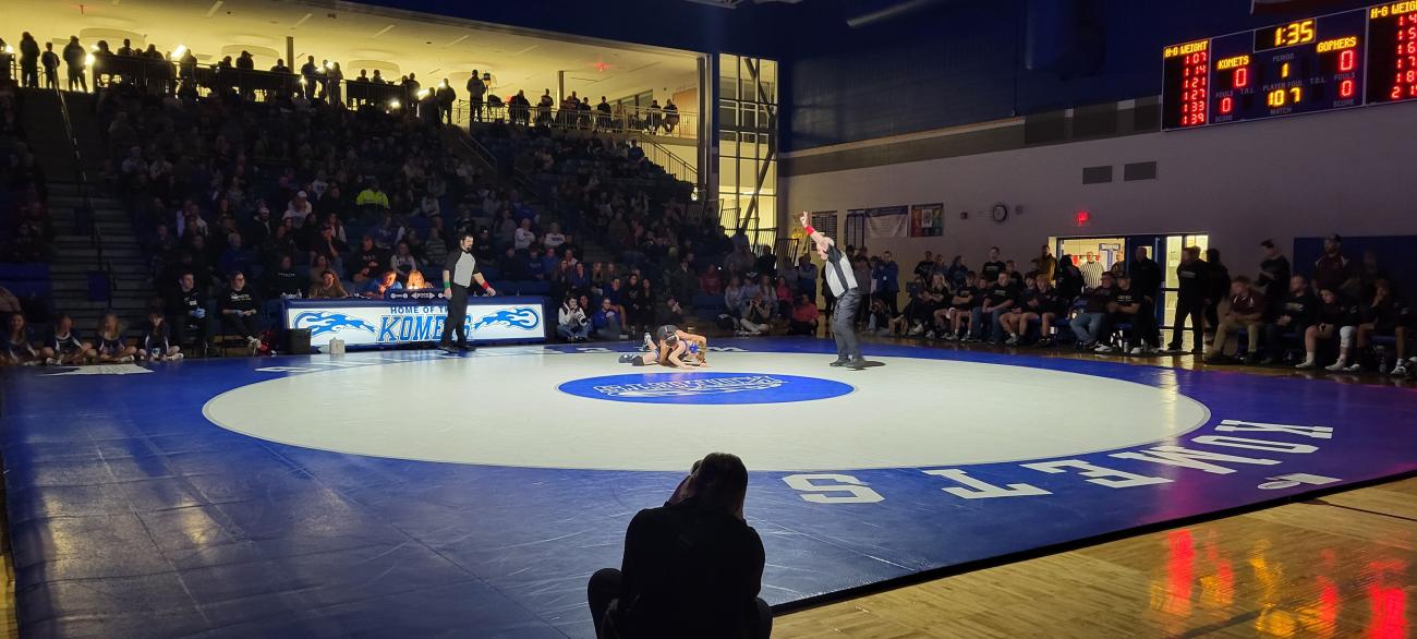 A spotlight shines on the Kasson-Mantorville mat during a high school wrestling match.